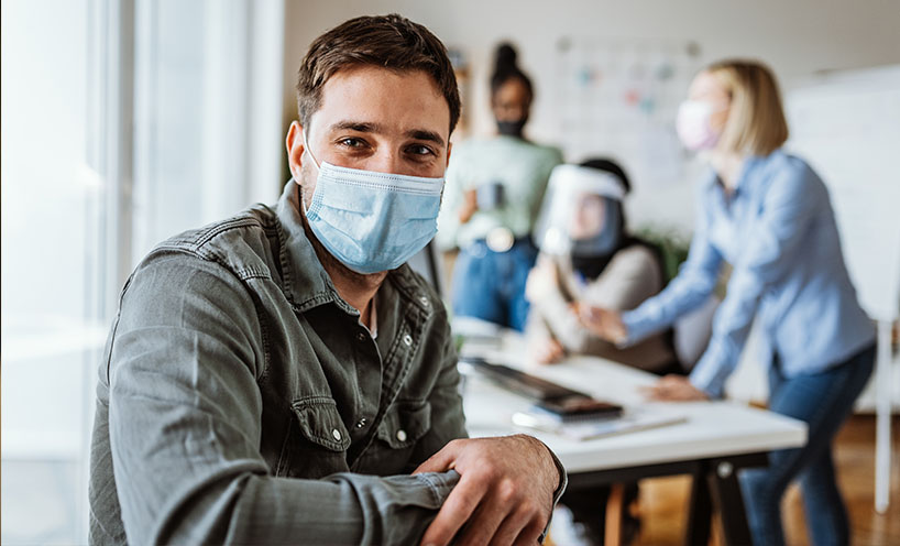 man in mask with team behind him at desk