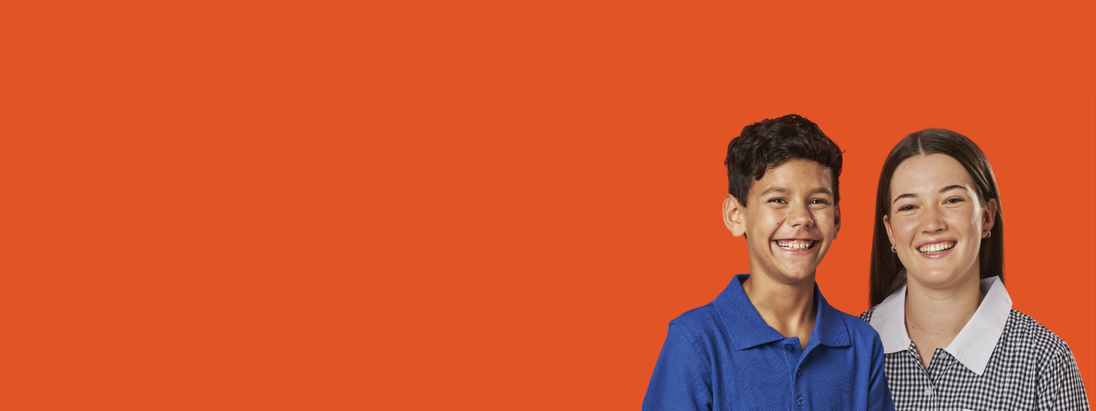 Two students in uniform smiling at the camera with orange background