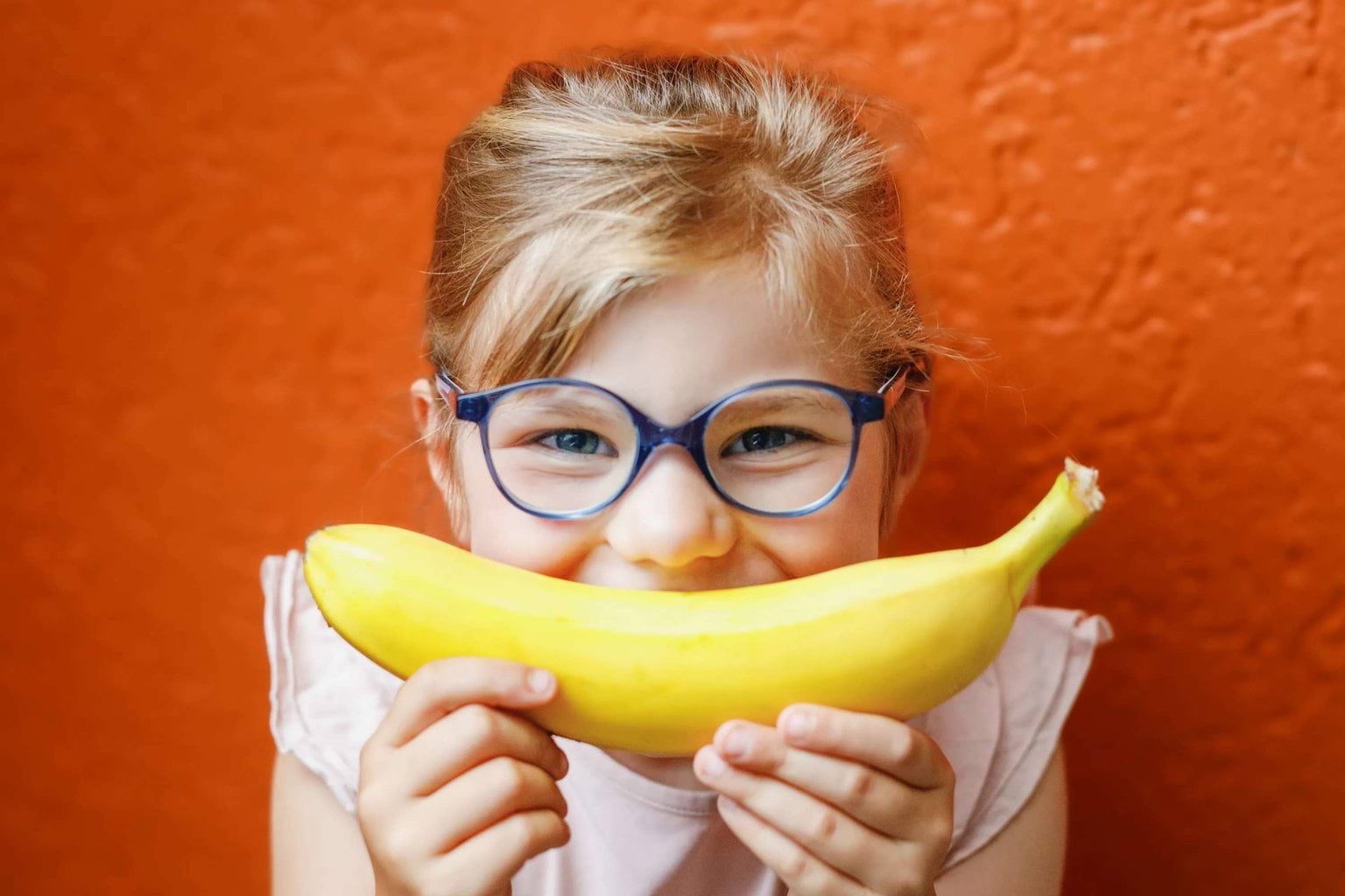 Girl smiling at camera, holding banana in front of her mouth