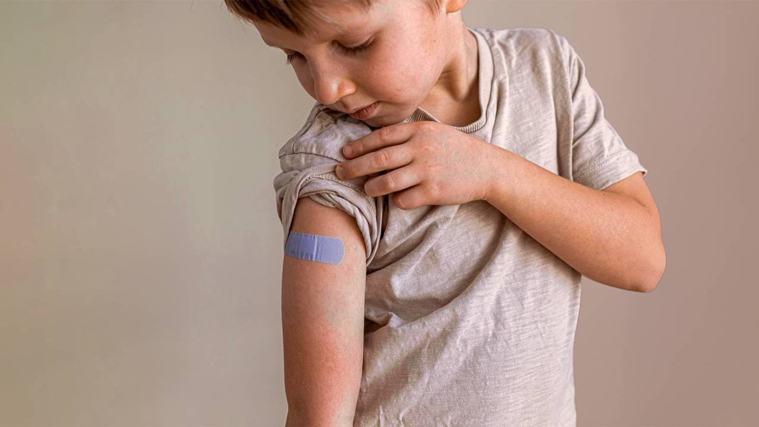 Boy looks at bandaid on arm after vaccination