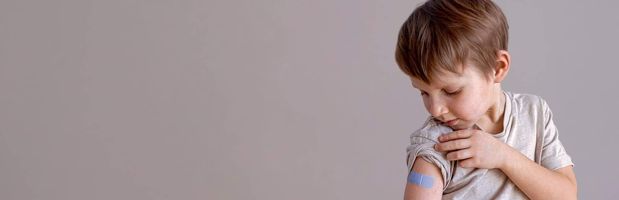 Boy looks at bandaid on arm after vaccination