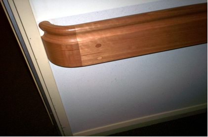 A wooden, rounded handrail in a corridor helps people with their mobility.